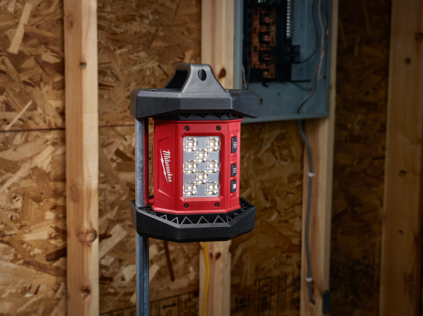 Compact red Milwaukee utility work light with multiple LEDs mounted on wooden wall studs near electrical panel
