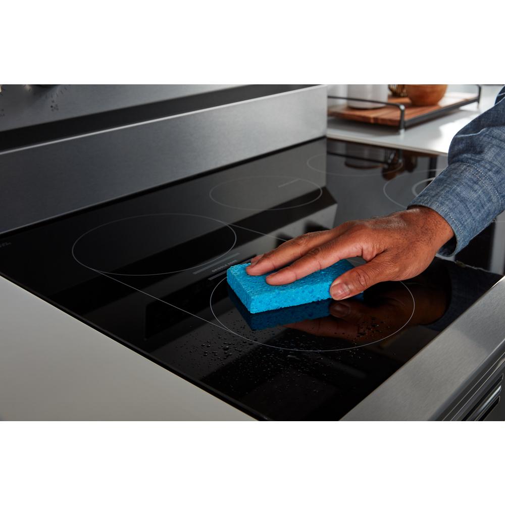 Hand cleaning a smooth black glass cooktop on a 30-inch electric range with a blue sponge in a modern kitchen.