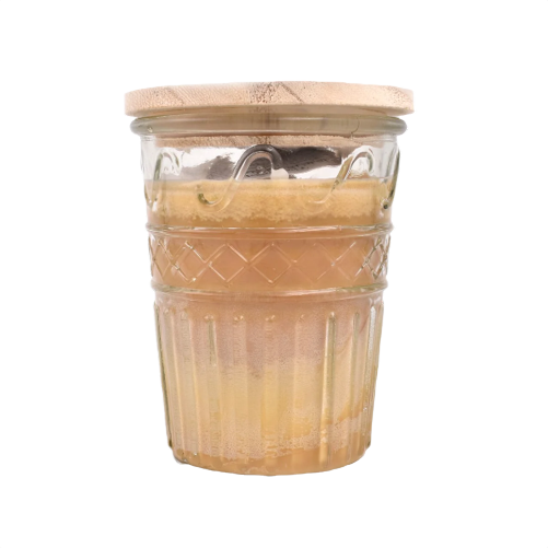 Glass jar candle with textured pattern and wooden lid filled with layered natural-colored wax