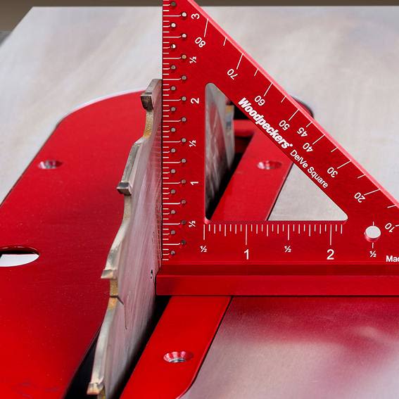 Red 3.5-inch aircraft-grade aluminum DelVe square measuring tool positioned on a table saw blade in woodworking tools collection