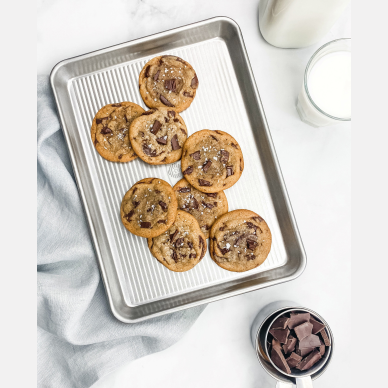 Aluminized quarter sheet pan with ribbed surface holding freshly baked chocolate chip cookies in kitchenware collection