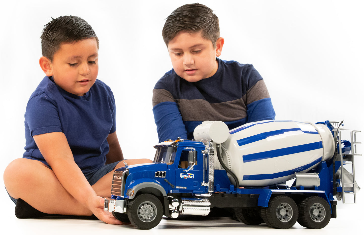 Two boys playing with a blue and white 1:16 scale Mack Granite cement mixer truck with rotating drum
