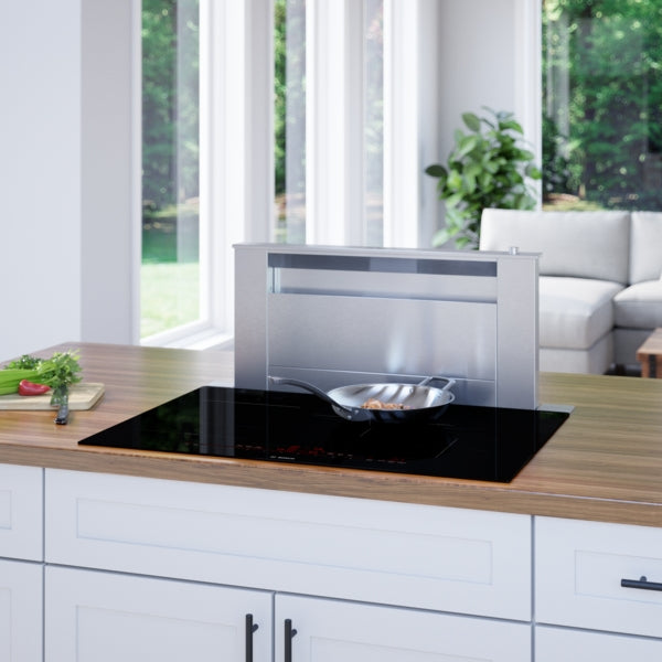 Modern induction cooktop with built-in downdraft vent and frying pan on a wooden kitchen counter in daylight