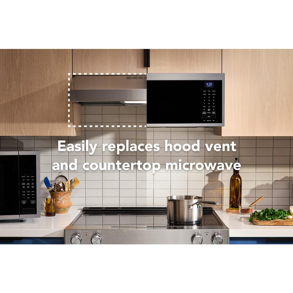 Under-cabinet stainless steel ventilation hood installed beside a black microwave in a modern kitchen setting