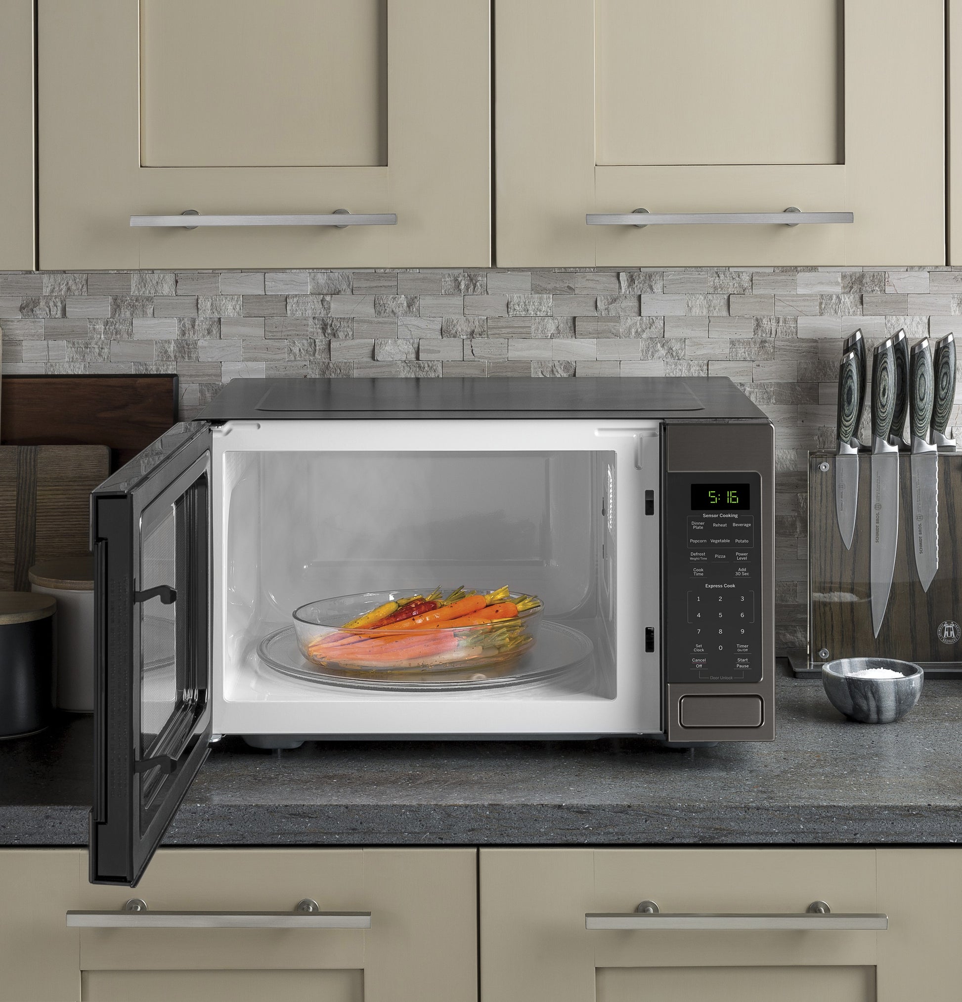 Countertop microwave oven in beige kitchen setting with digital display and open door showing a glass dish with food