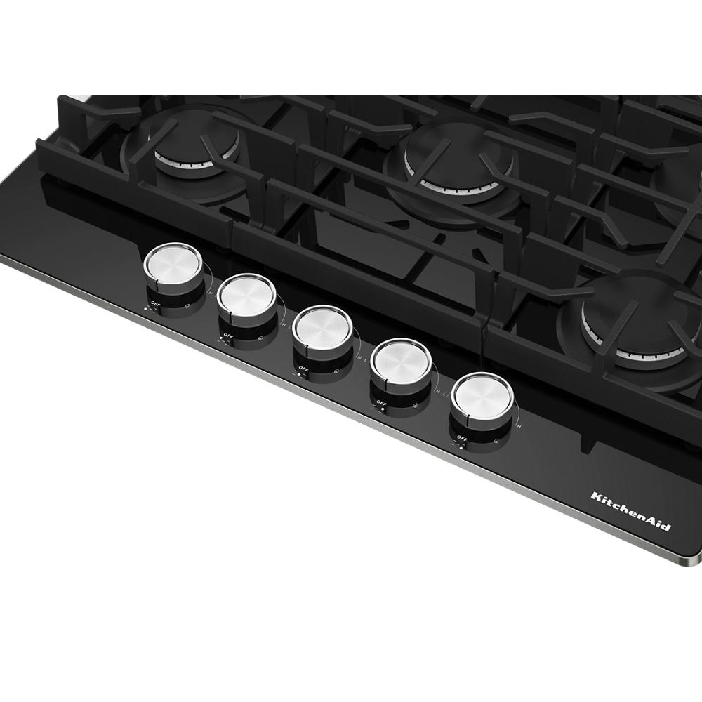 Black glass cooktop surface with five silver control knobs and cast iron grates for kitchen appliances and home improvement collections