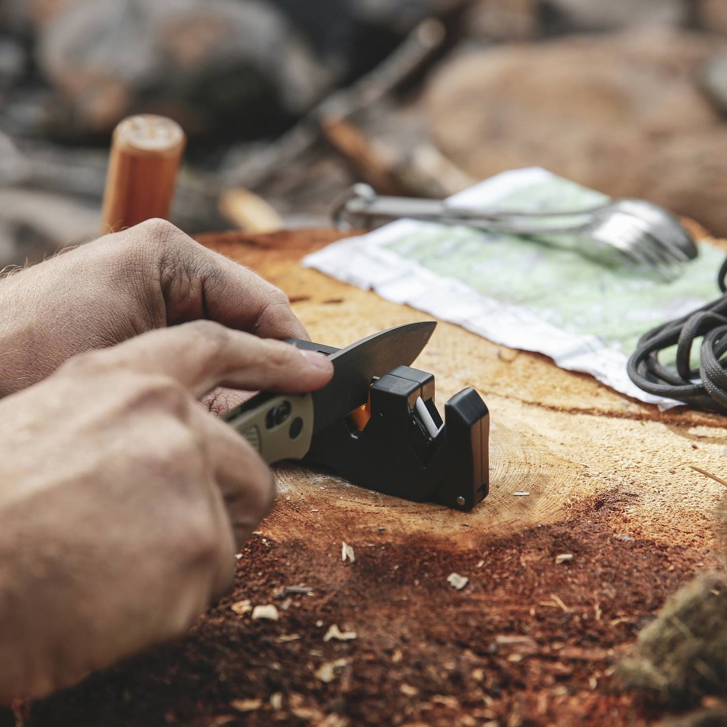 Person sharpening a folding knife using a compact sharpener on a wooden stump for outdoor tool maintenance