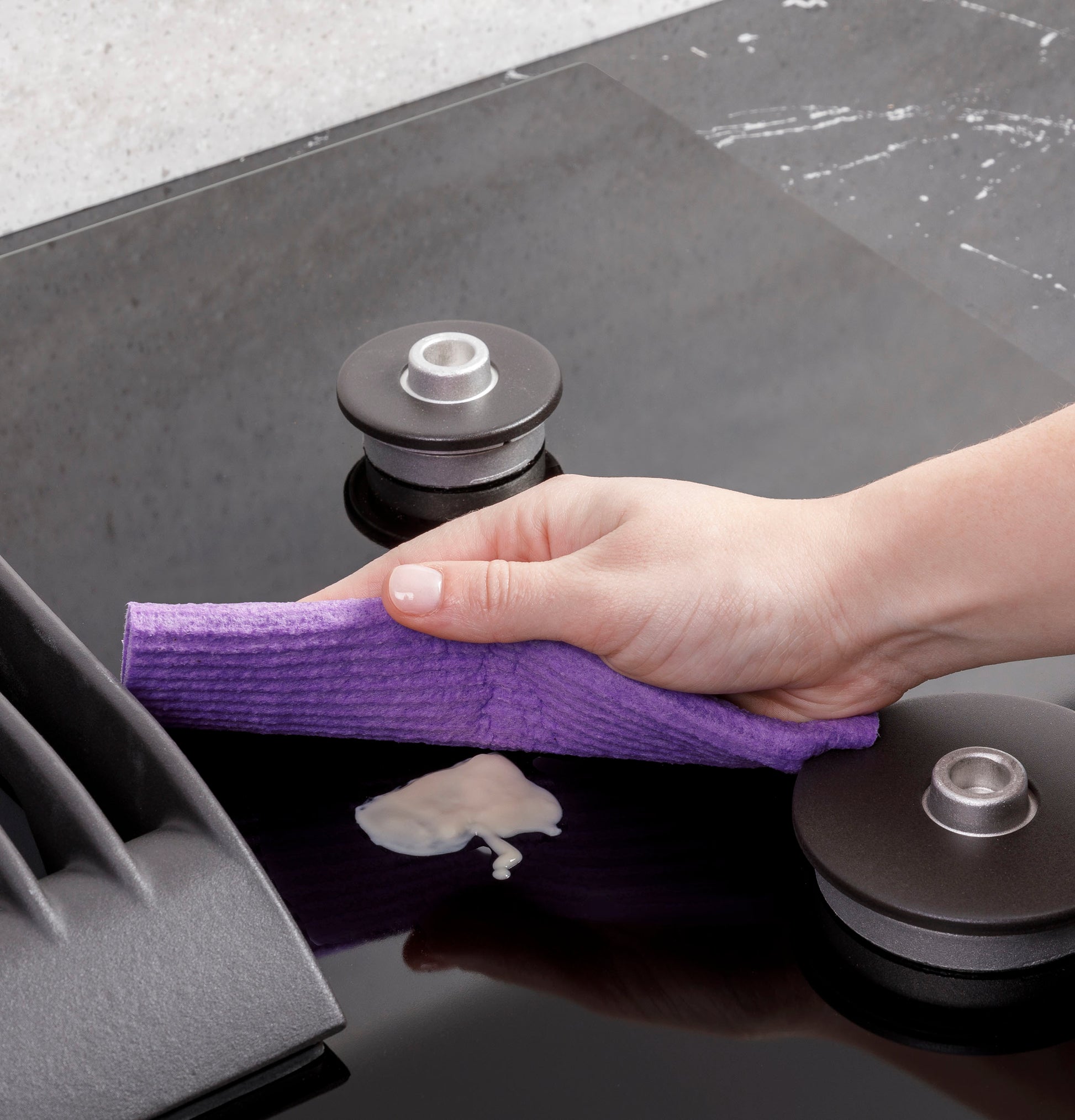 Hand wiping spill on sleek black surface of built-in gas downdraft cooktop in modern kitchen setting