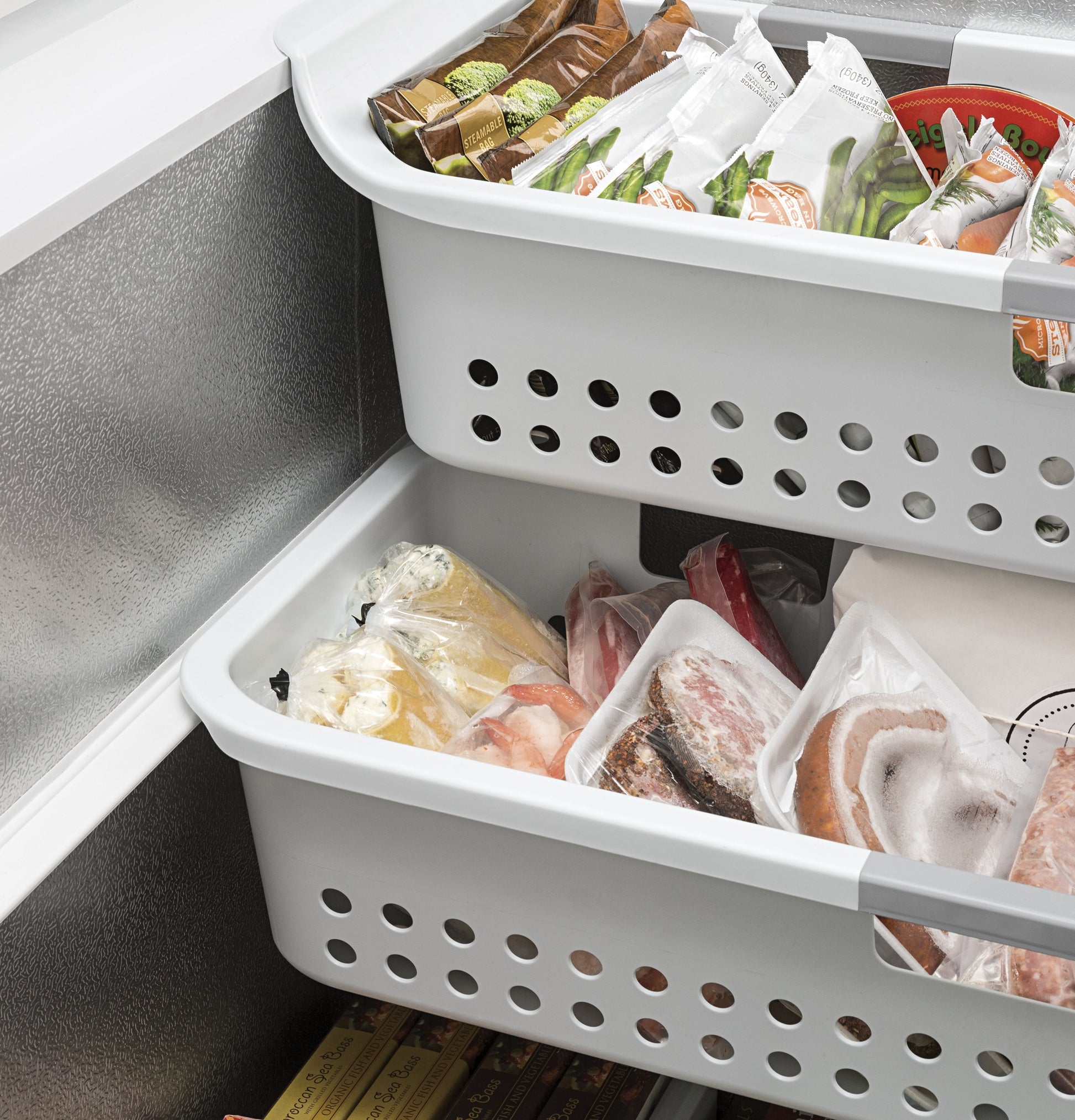 Two white storage baskets with assorted frozen foods inside a manual defrost chest freezer for kitchen and home appliances.
