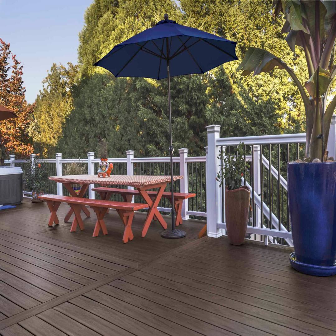 Outdoor deck with dark wood grain riser boards, picnic table, blue umbrella, and white railing for home improvement projects