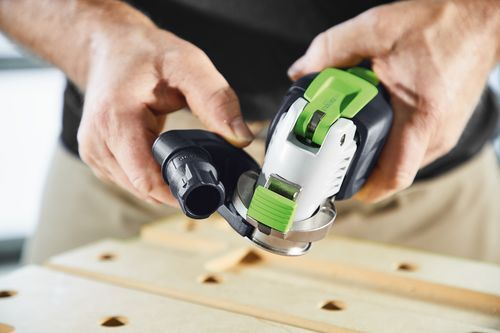 Hands securing a green and black cordless oscillator tool over a wooden workbench for home improvement tasks