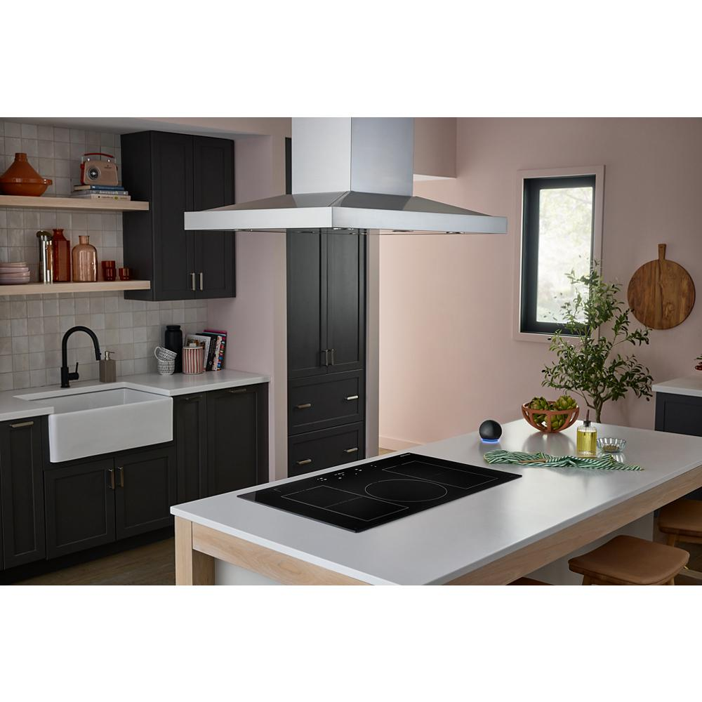 Modern kitchen with black induction cooktop centered on white island beside dark cabinetry and farmhouse sink