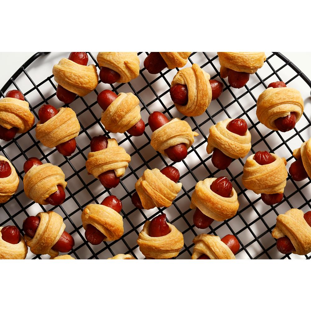 Mini crescent rolls wrapped around cooked cocktail sausages cooling on a wire rack in kitchenware setting