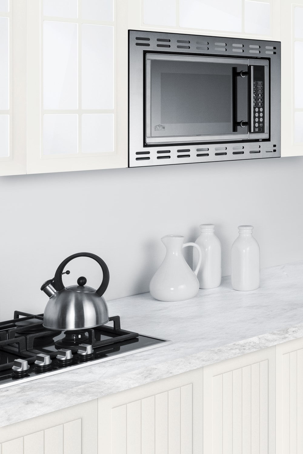 Built-in stainless steel microwave with digital controls above white countertop featuring a gas stove and ceramic pitchers