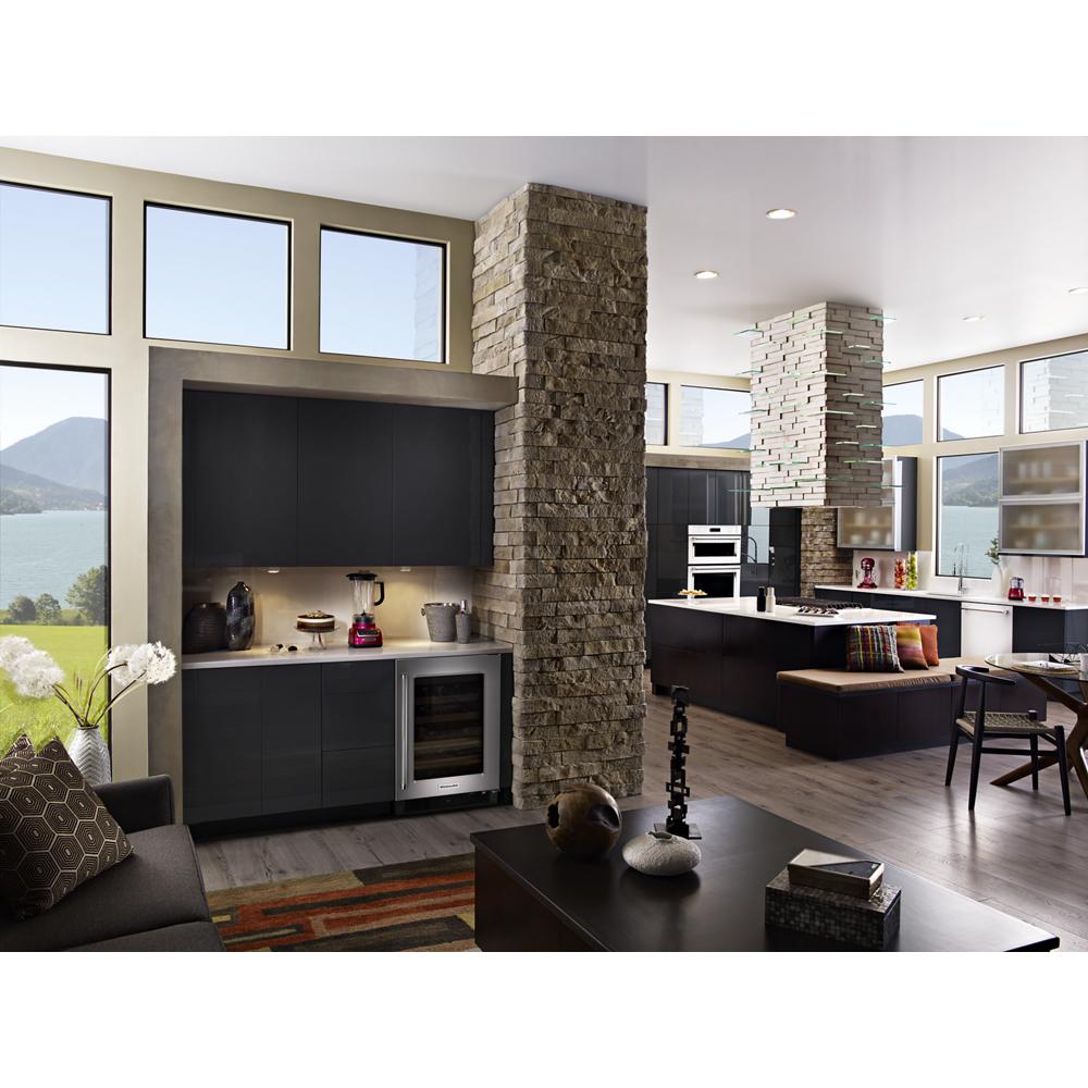 Contemporary kitchen with dark cabinetry, stone pillars, large windows, and stainless steel island-mount canopy hood from KitchenAid collection