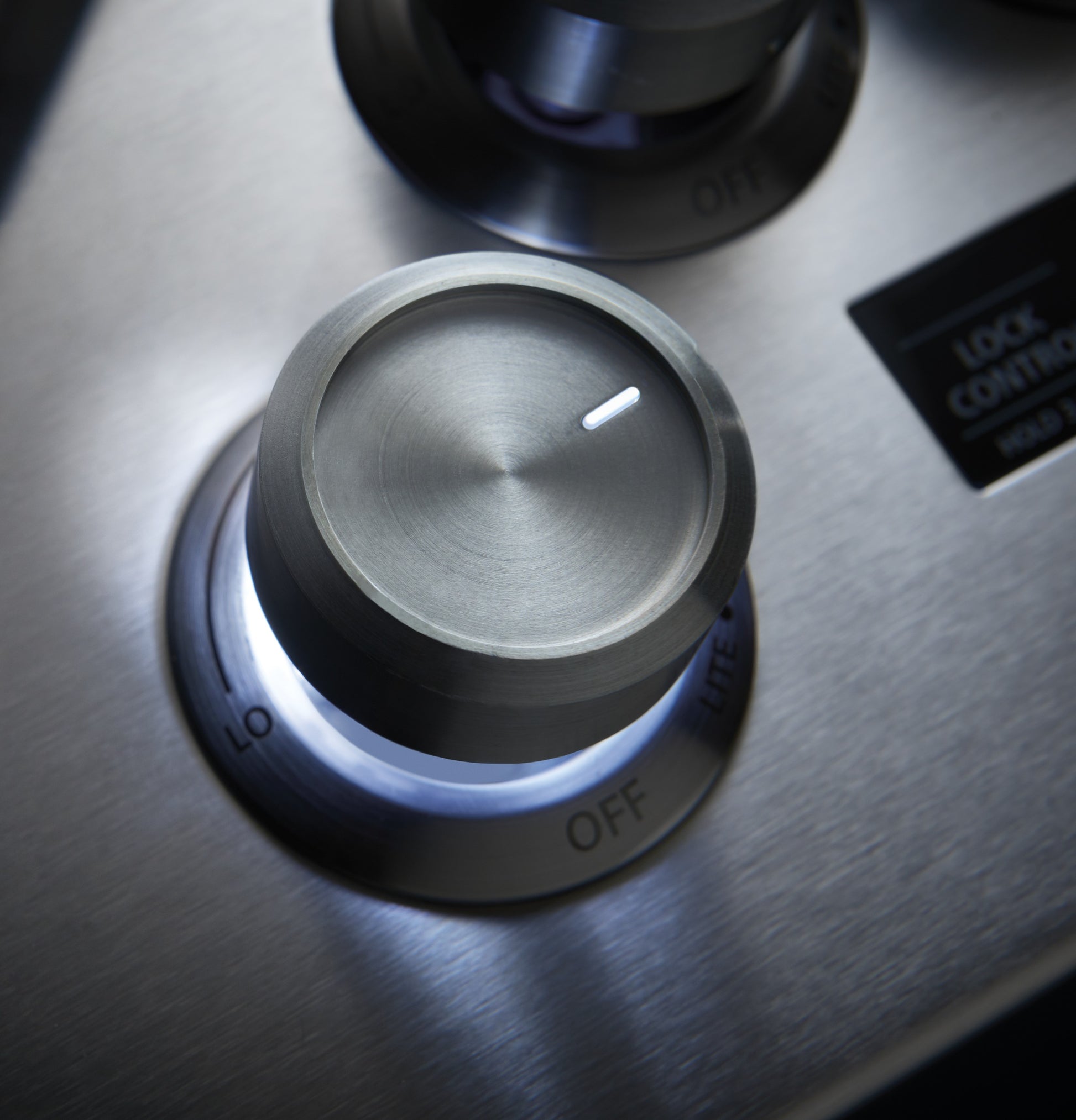Close-up of brushed stainless steel burner control knob on Monogram deep-recessed gas cooktop in kitchenware setting