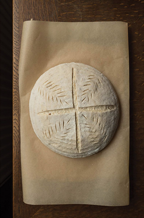 Round artisan bread with detailed scoring pattern on parchment paper in kitchenware and bakeware collections