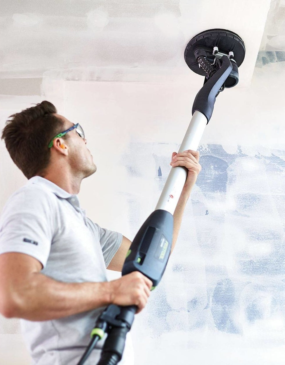 Person using Festool drywall sander to smooth ceiling surface in home improvement and power tools setting