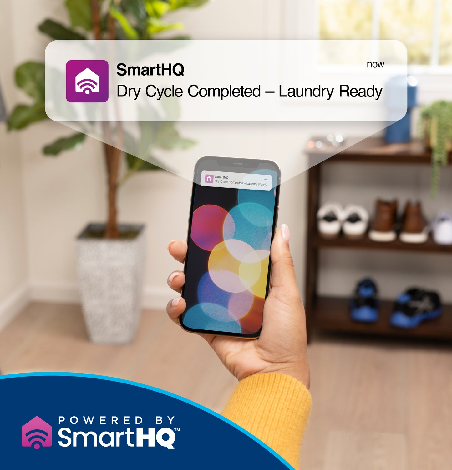 Hand holding smartphone displaying SmartHQ notification for completed dry cycle in modern laundry room setting