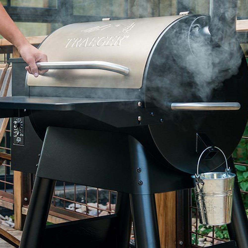 Person opening a smoking outdoor grill with metal grease bucket attached for tools and home improvement use