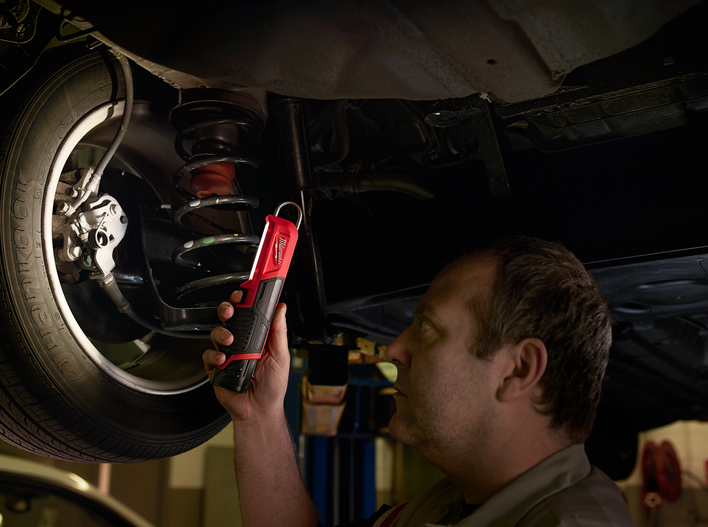 Man inspecting vehicle suspension using compact Milwaukee M12™ Stick Light in automotive repair workshop
