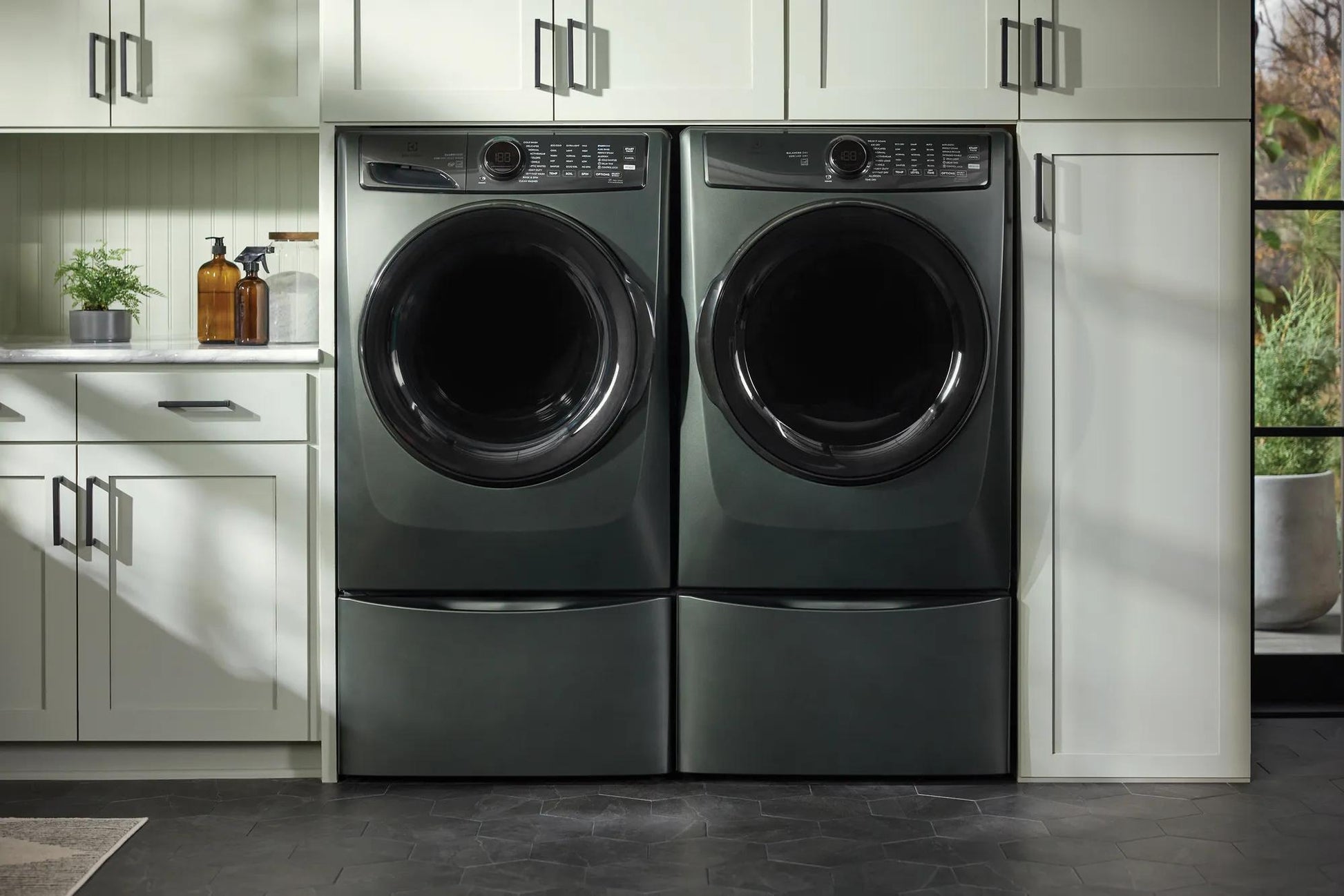 Pair of dark front-load washer and dryer units elevated on sleek storage pedestals in a modern laundry room setting