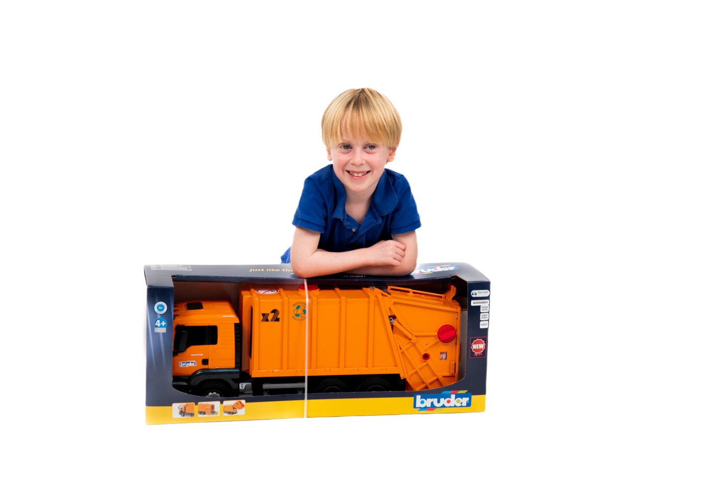 Young boy in blue shirt smiling while leaning on boxed Bruder MAN TGS orange toy garbage truck for playtime