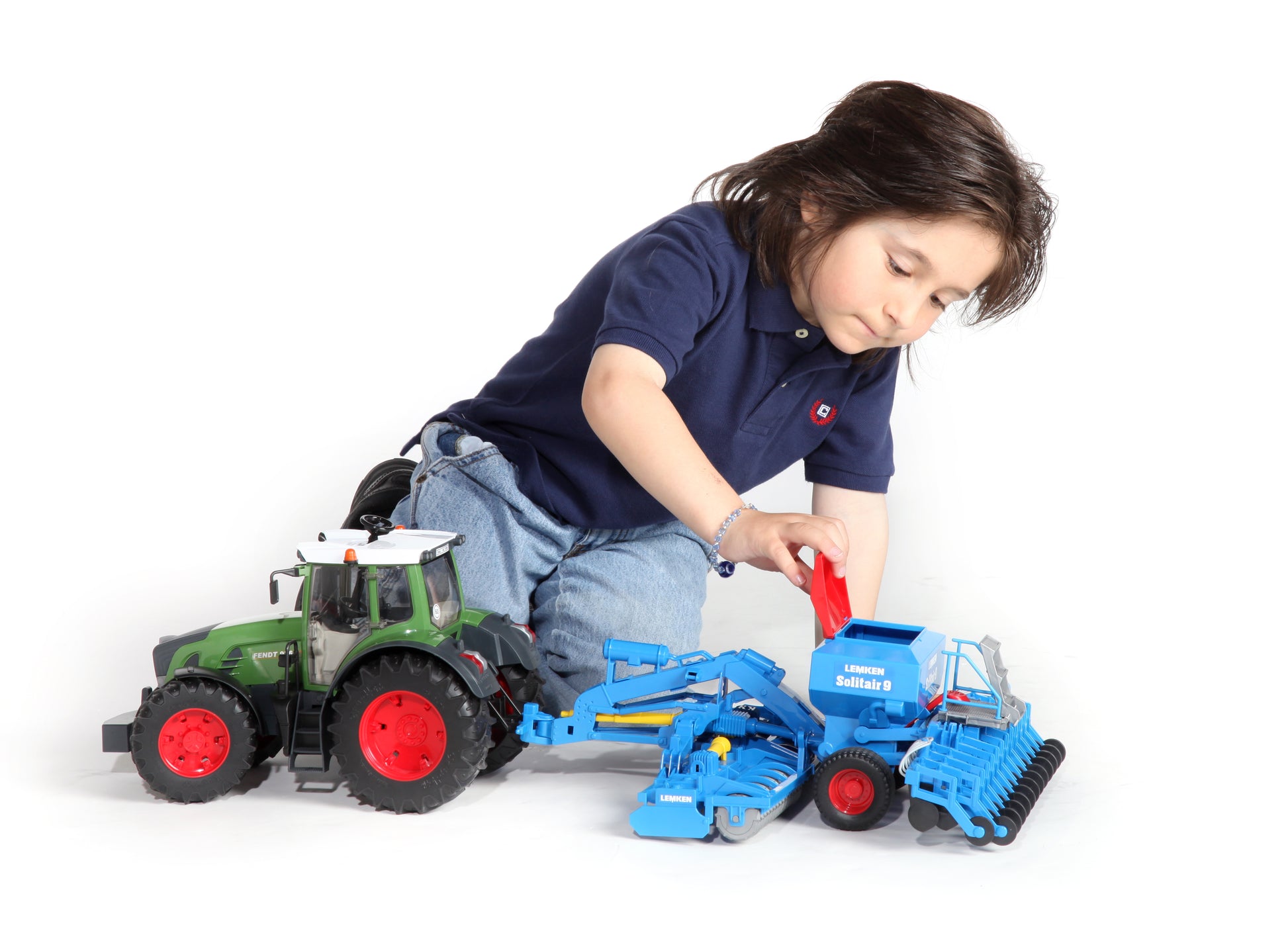 Young child playing with green tractor toy attached to blue Bruder Lemken Solitair 9 sowing combination model