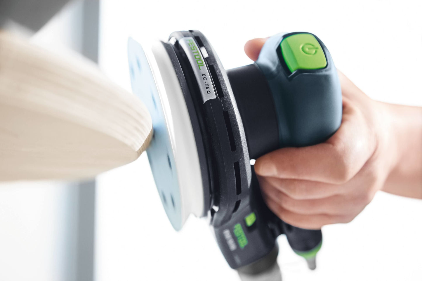 Handheld Festool orbital sander smoothing the edge of a wooden surface in a woodworking environment