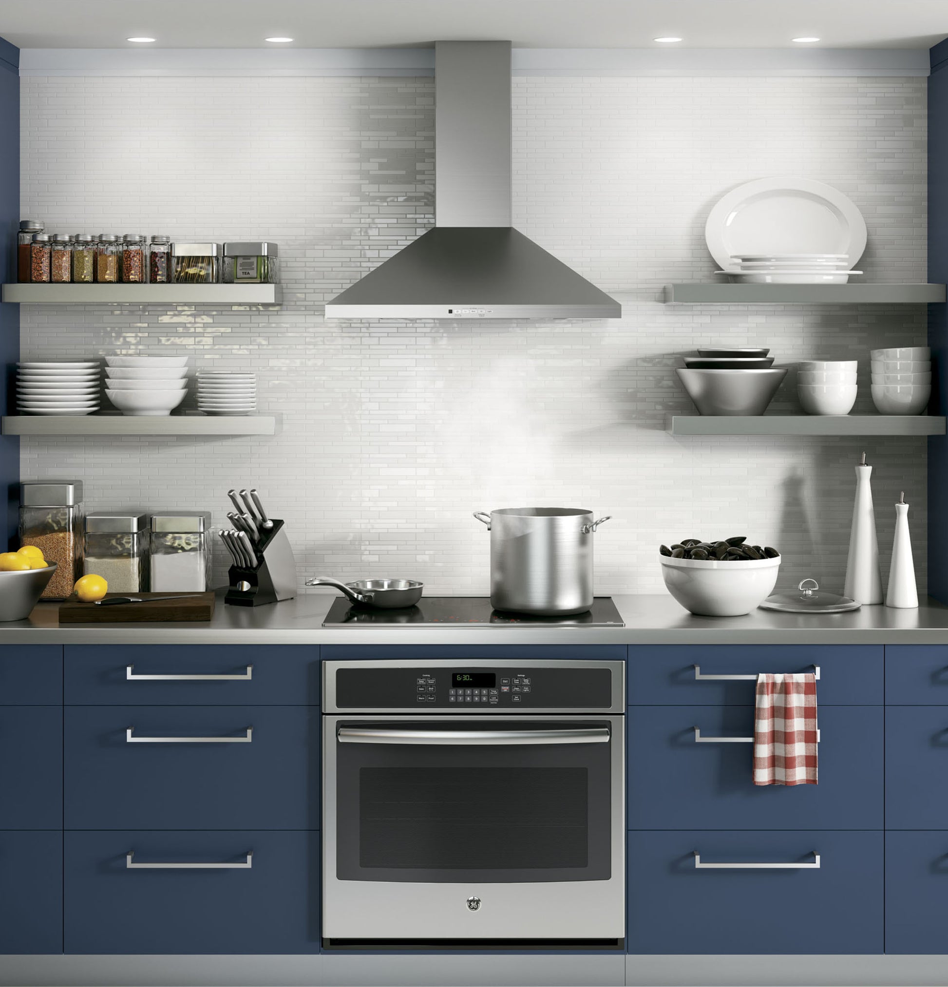 Modern stainless steel wall-mounted pyramid chimney hood above electric range in contemporary kitchen setting with blue cabinetry
