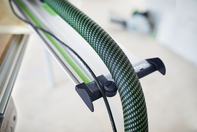 Close-up of fastening clamp and angle stop on Festool guide rail accessory with green and black textured hose nearby