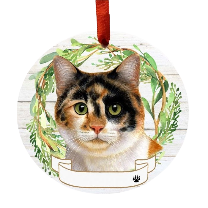 Round Christmas ornament featuring a calico cat face framed by a green foliage wreath and red ribbon hanger