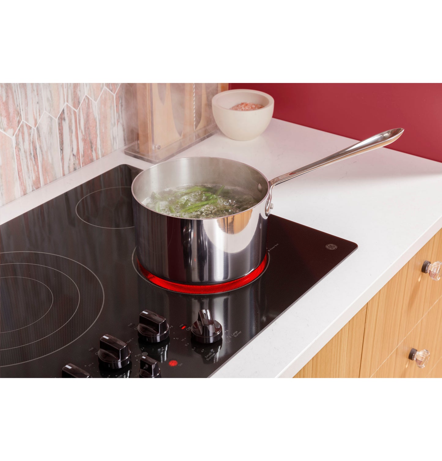 Stainless steel pot boiling water on black built-in electric cooktop with knob controls in kitchen setting