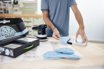 Person organizing blue sanding discs and accessories from a Festool Granat sanding disc starter set for home improvement tasks