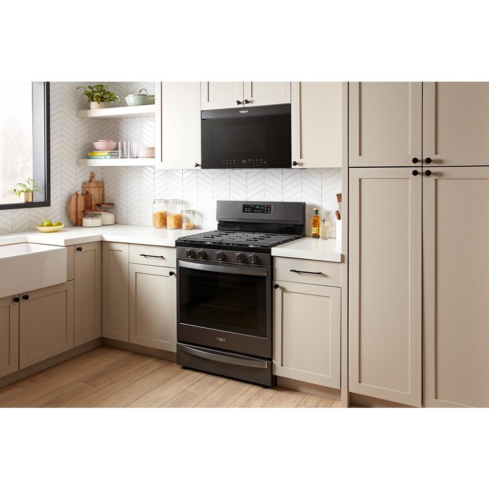 Kitchen with black over-the-range microwave and freestanding oven surrounded by light beige cabinetry and wood floor