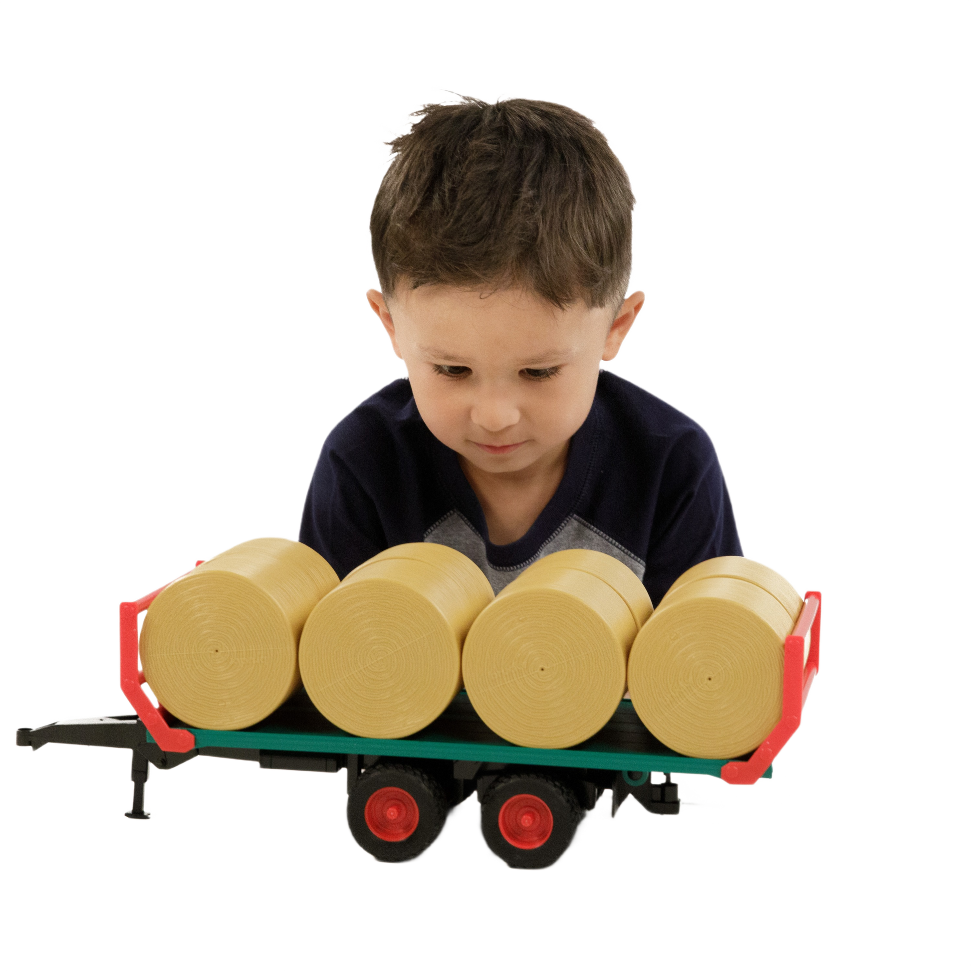 Young boy focused on green and red bale trailer loaded with four round bales for imaginative farm play and home improvement tools.