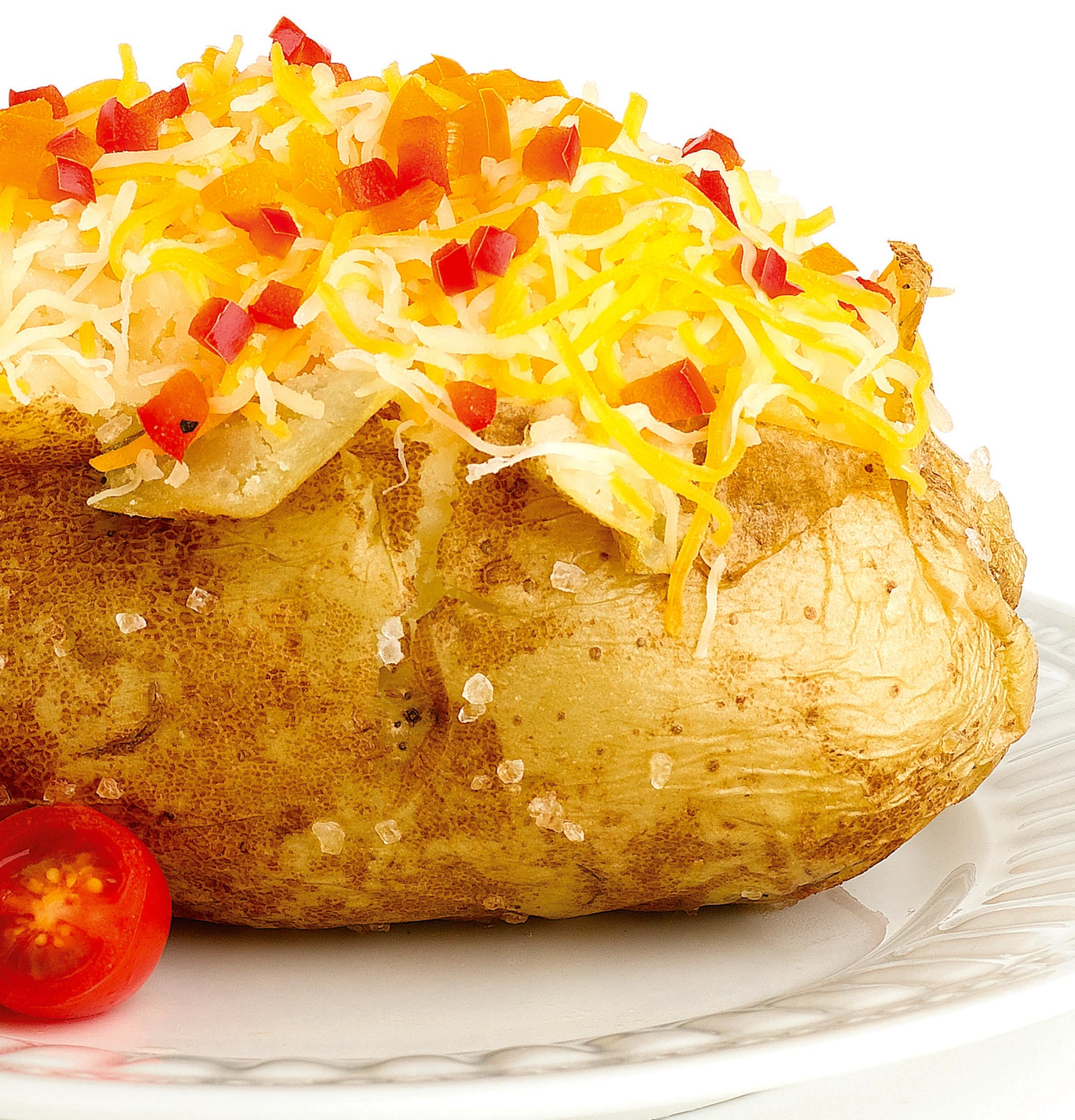 Baked potato topped with shredded cheese and diced red peppers on white plate with cherry tomato half