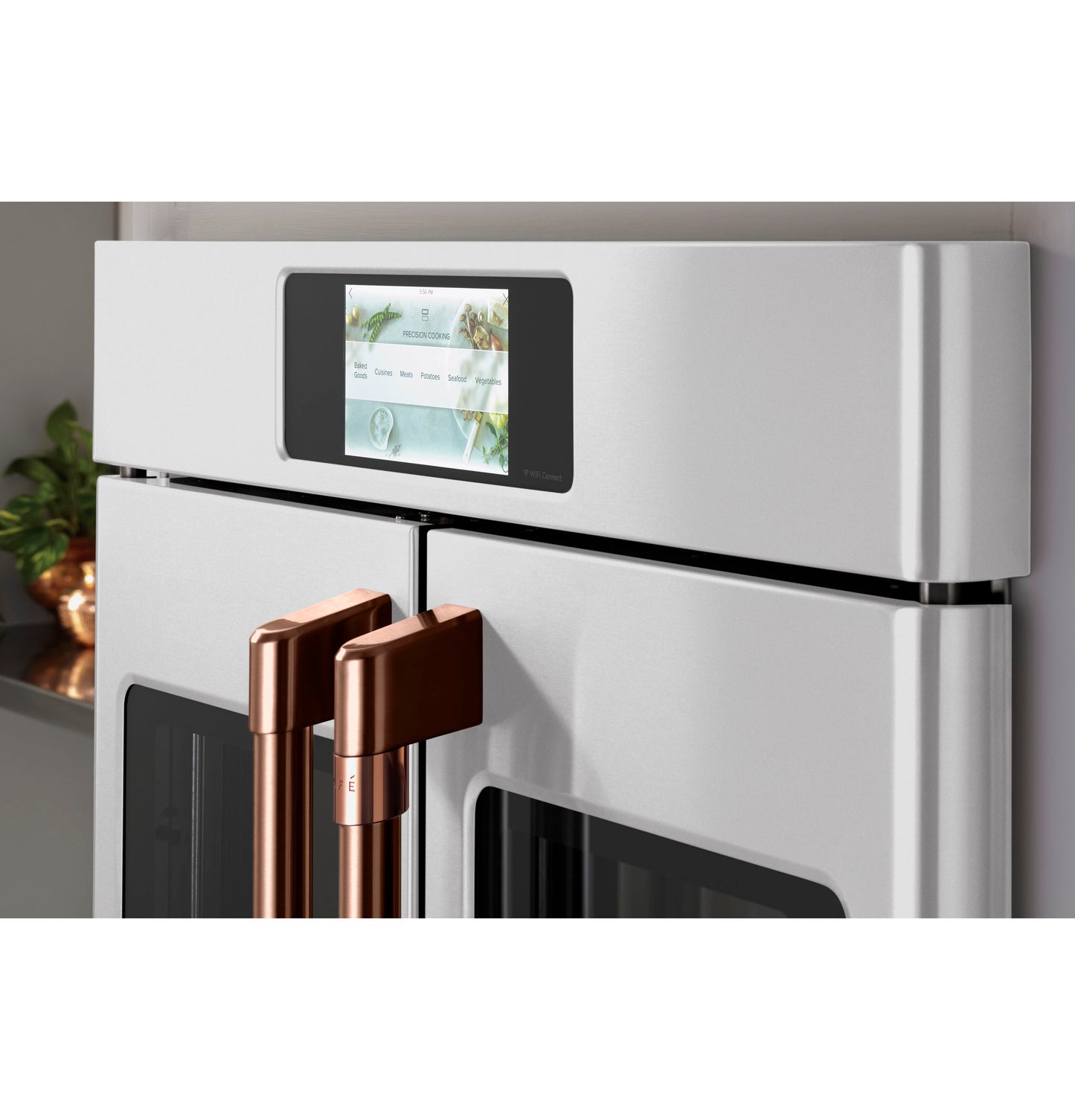 Close-up of white built-in French-door convection wall oven with digital touchscreen and copper metal handles in kitchen setting