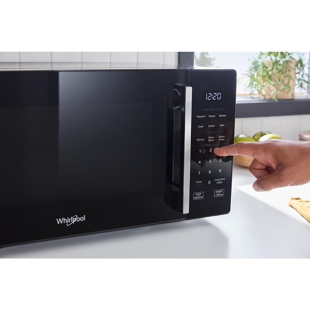 Black countertop microwave with digital touchpad and LED display being operated in bright kitchen setting