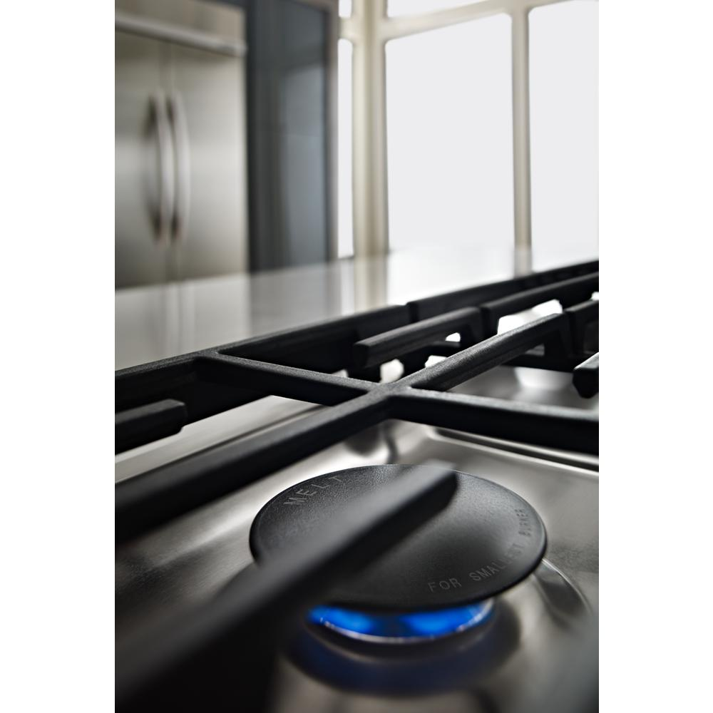 Close-up of blue flame burning on stainless steel gas burner with black cast iron grate in modern kitchen setting