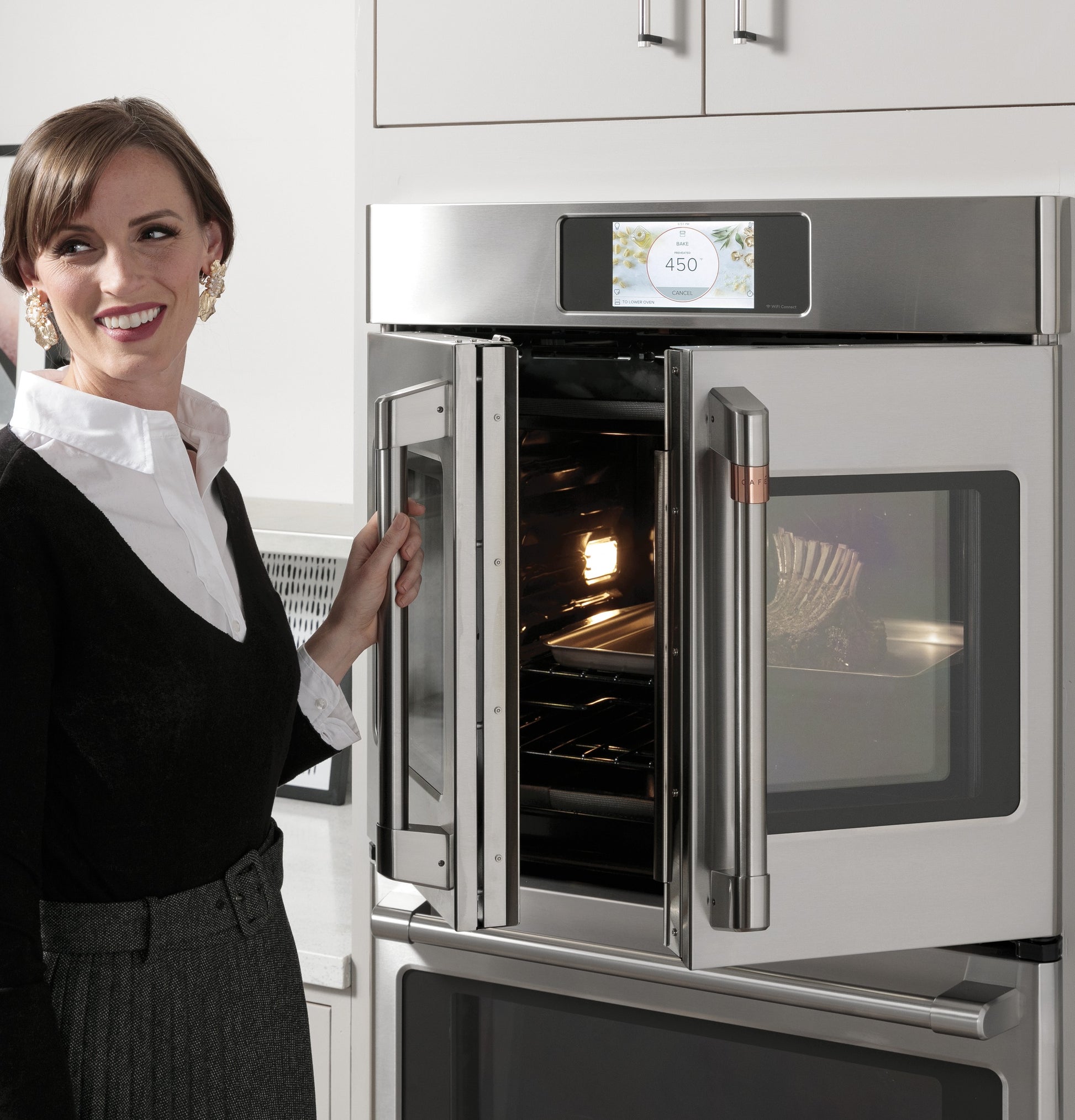 Woman opening stainless steel built-in convection wall oven with touchscreen in modern kitchen setting