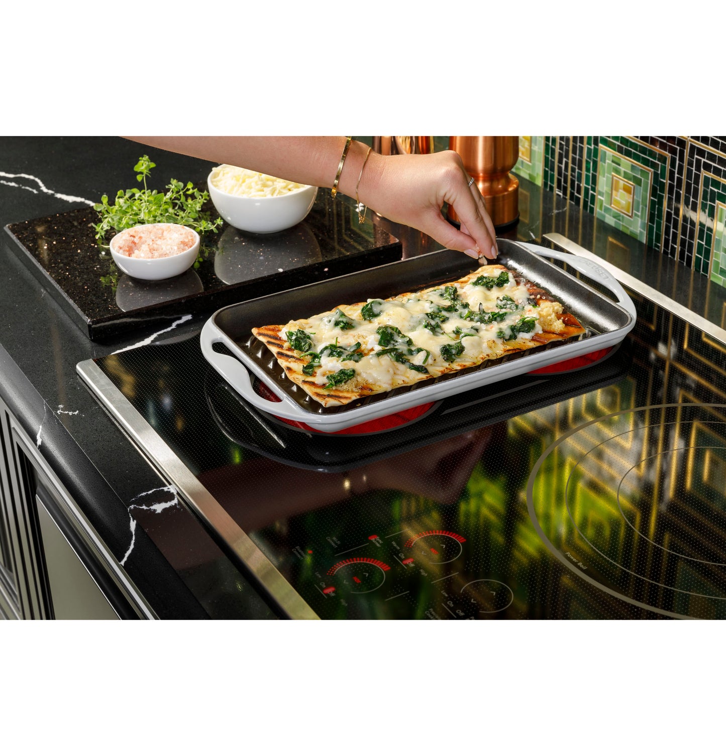 Close-up of a ceramic dish with cooked spinach and cheese on a modern black electric cooktop in a stylish kitchen setting