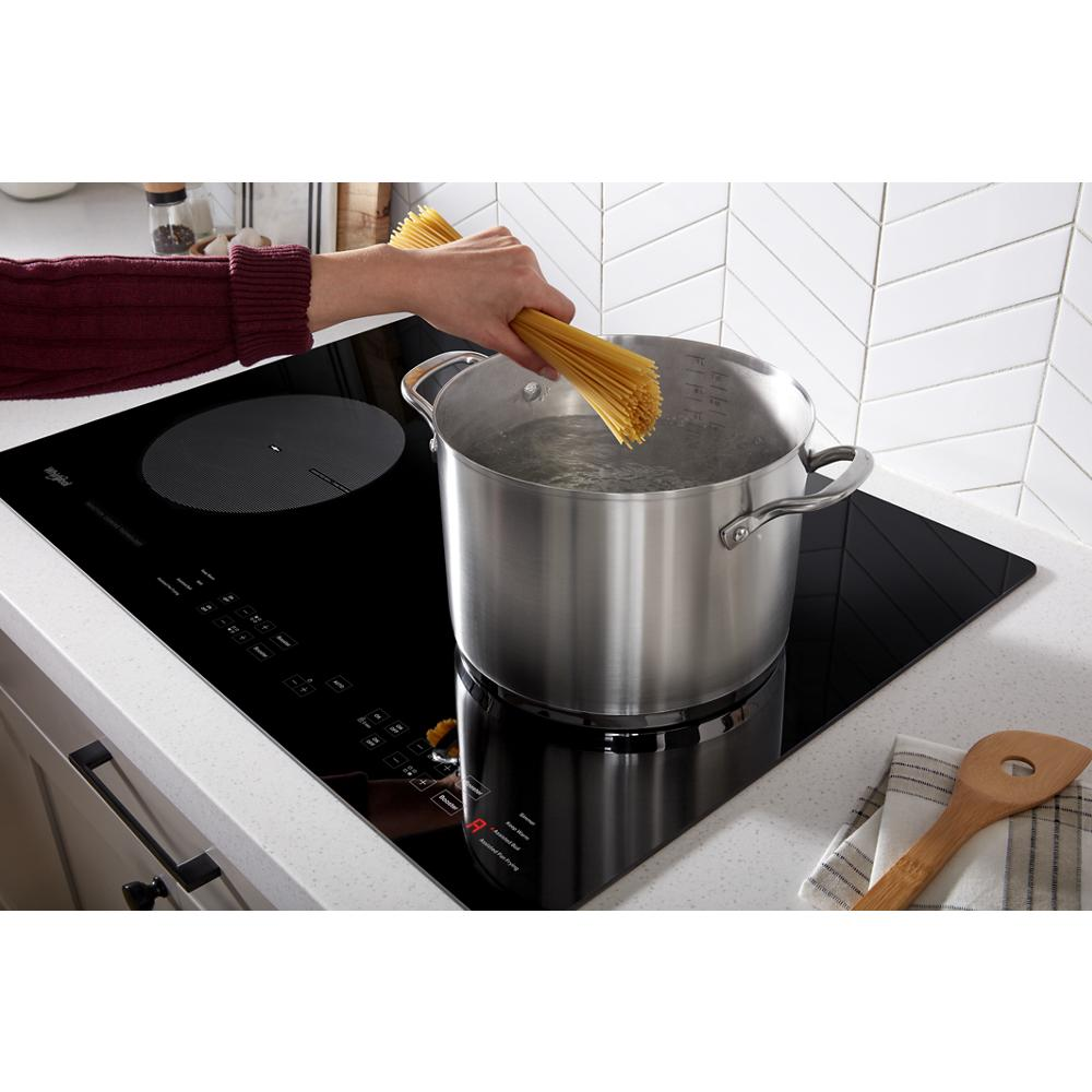 Modern black induction cooktop with touch controls boiling water in stainless steel pot, kitchenware and appliances setting