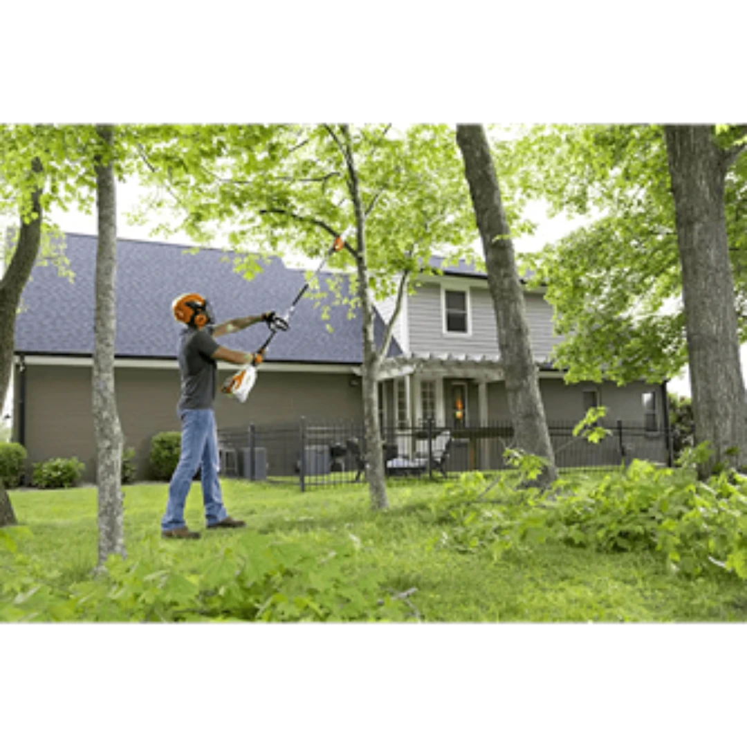 Person using a pole pruner attachment on a tree in a residential yard for trimming and home improvement tools