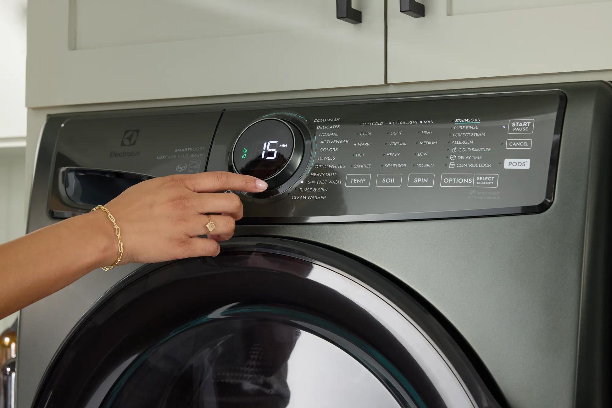 Close-up of hand adjusting dial on dark gray front load washer control panel in modern laundry setting
