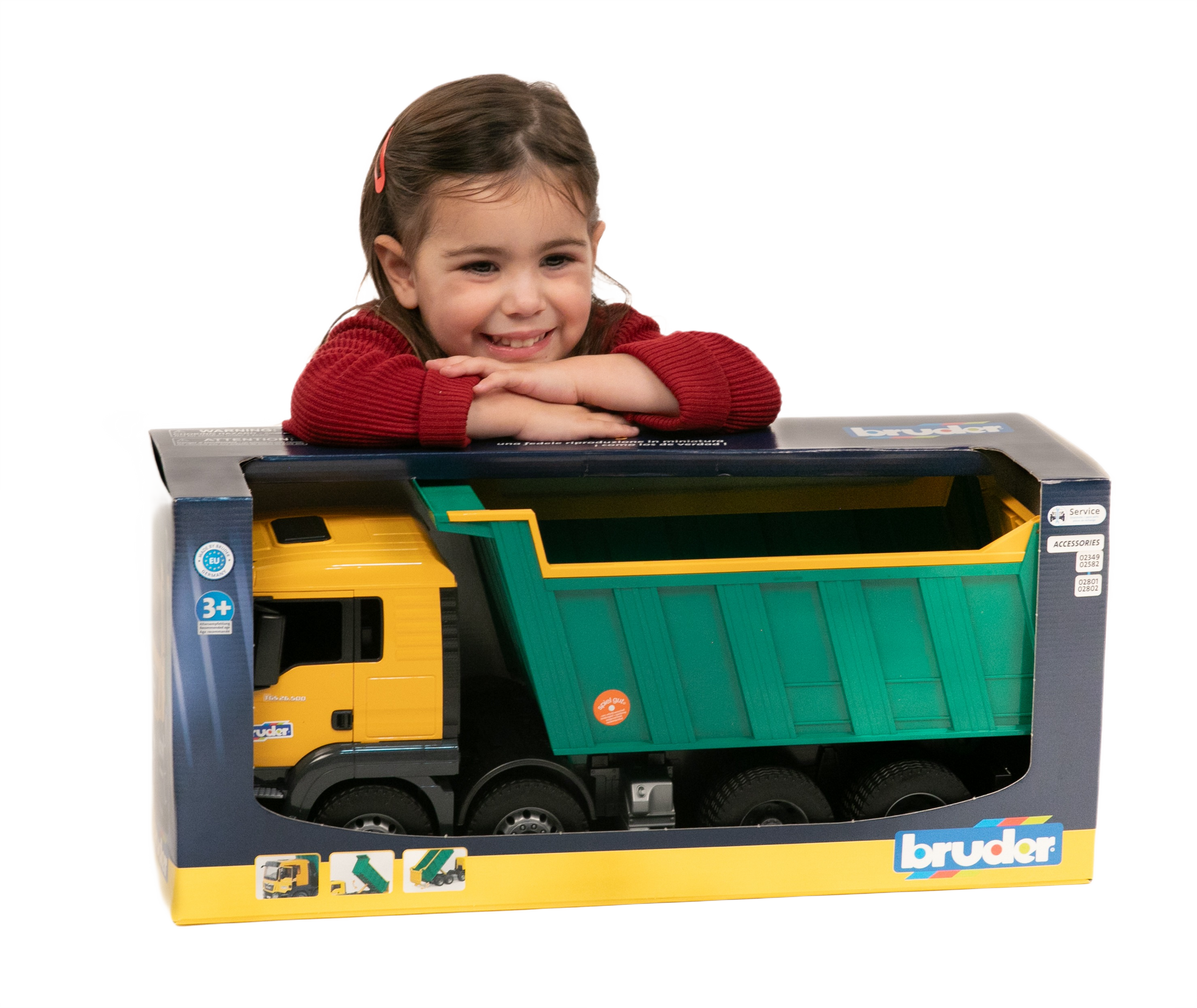 Child smiling while leaning on boxed Bruder Man Dump Truck toy with yellow cab and green dump bed