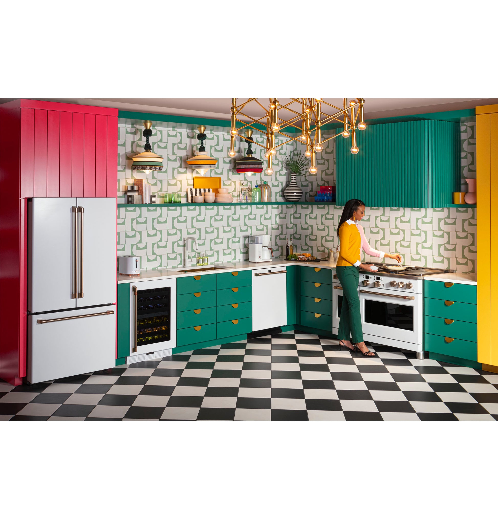 Woman cooking in colorful kitchen with teal and yellow cabinets, black and white checkered floor, and gold chandelier