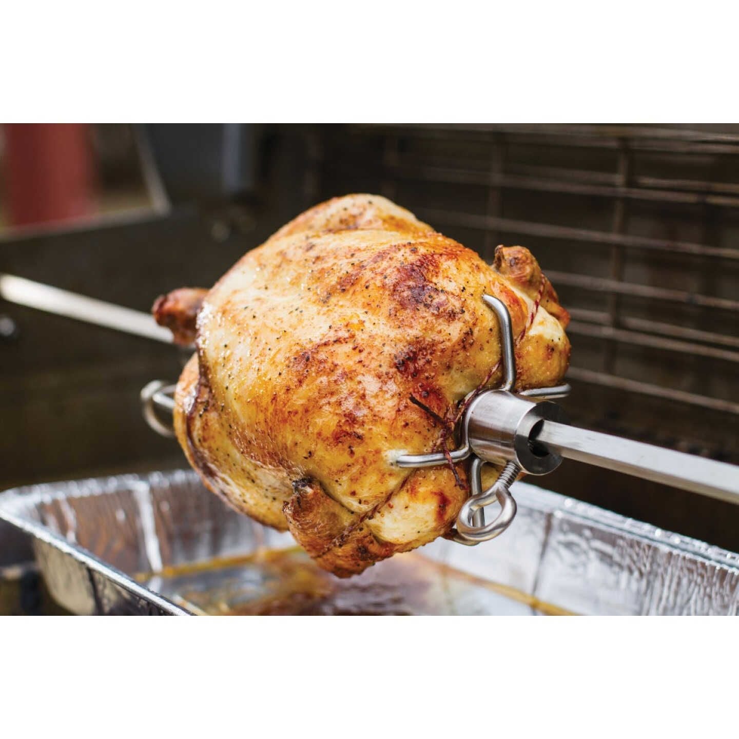 Rotisserie chicken cooking on a stainless steel spit over a drip tray in a home improvement setting