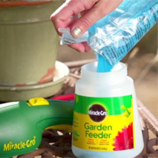 Hand pouring blue water-soluble plant food into a garden feeder container for plant care and lawn use