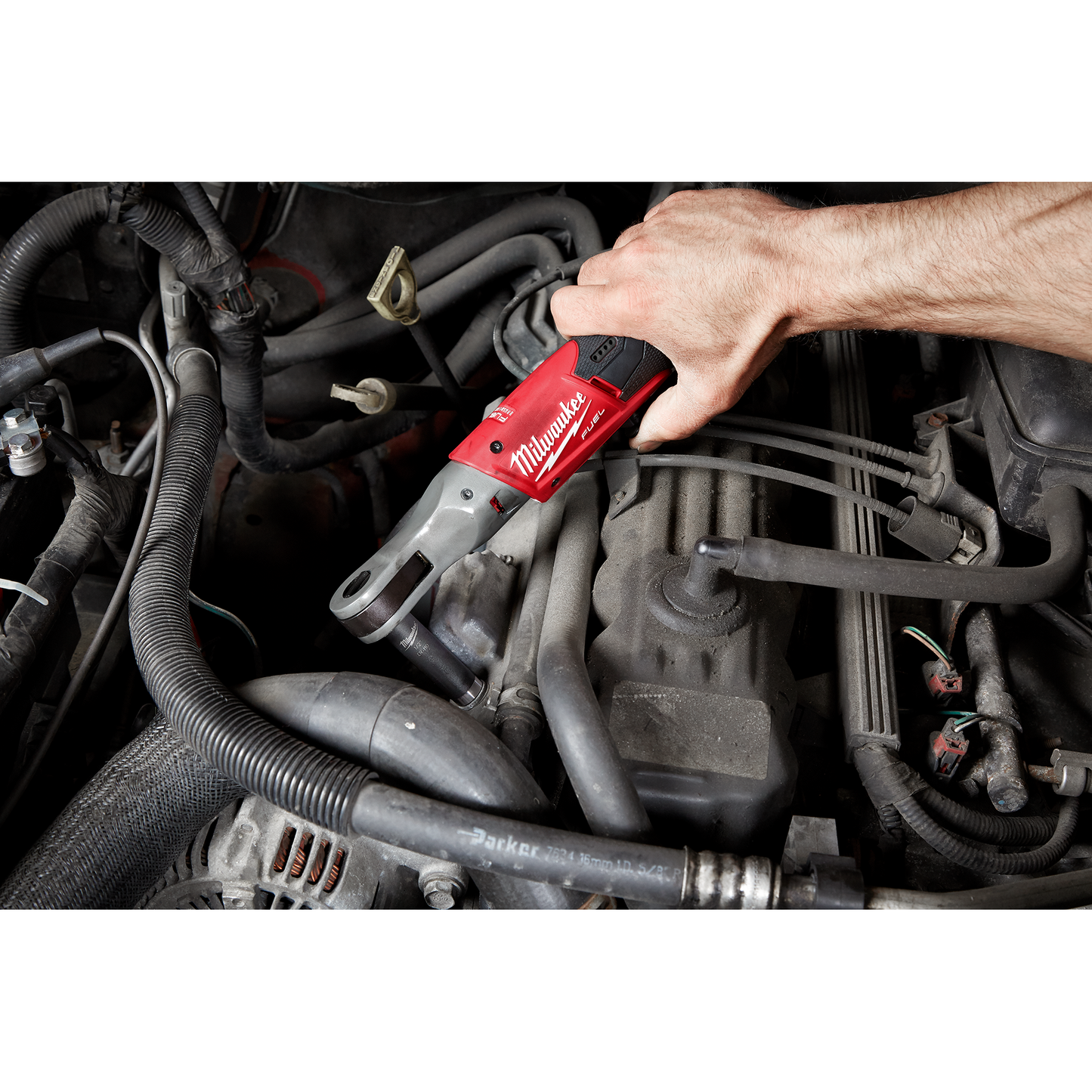Hand operating a red cordless ratchet wrench on a car engine for automotive repair and home improvement tasks